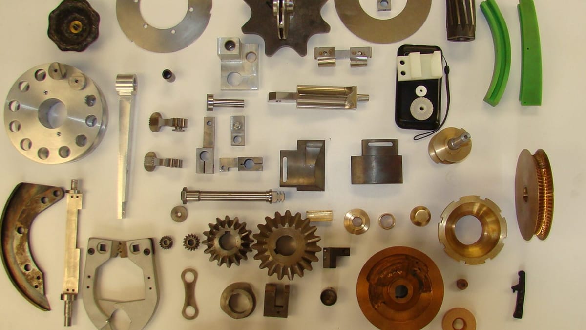 Overhead view of assorted machined parts on a white background: discs, sprockets, flanges, bronze bevel gears, bushings and nylon components.